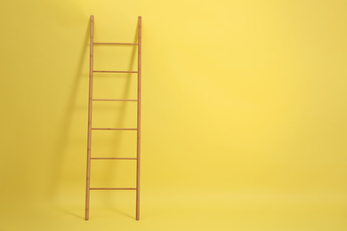 Photo of Modern wooden ladder on yellow background. Space for text
