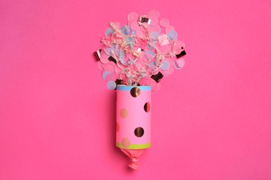 Beautiful serpentine and confetti bursting out of party popper on pink background, flat lay