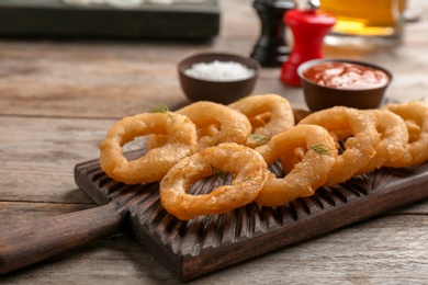 Photo of Wooden board with fried onion rings on table