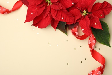 Photo of Flat lay composition with poinsettias (traditional Christmas flowers) and ribbon on beige background. Space for text