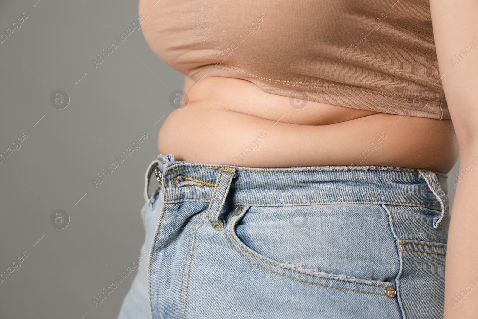 Photo of Overweight woman in tight jeans on grey background, closeup. Space for text