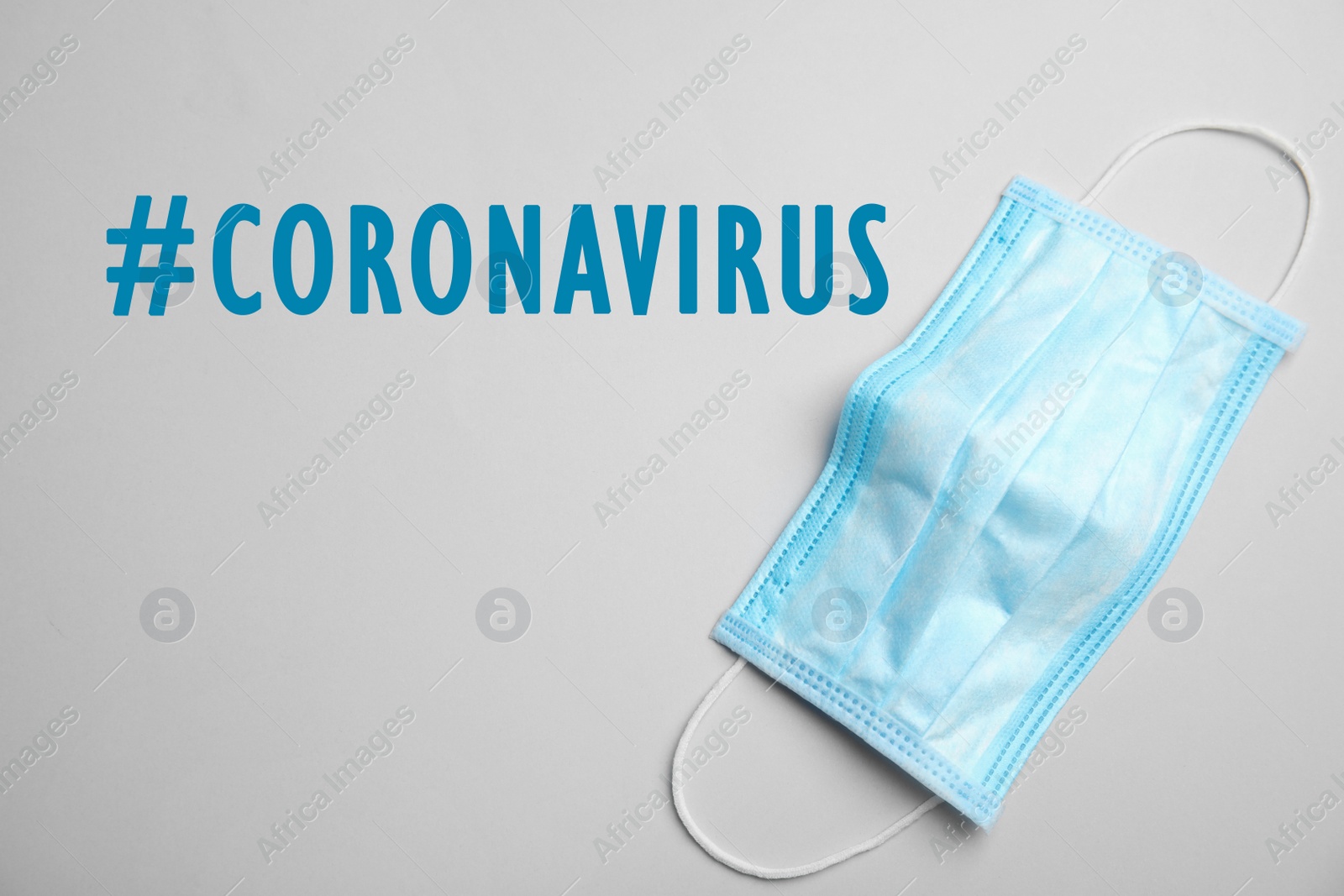 Image of Hashtag Coronavirus and medical mask on light background, top view