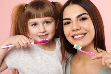 Photo of Little girl and her mother brushing teeth together on color background