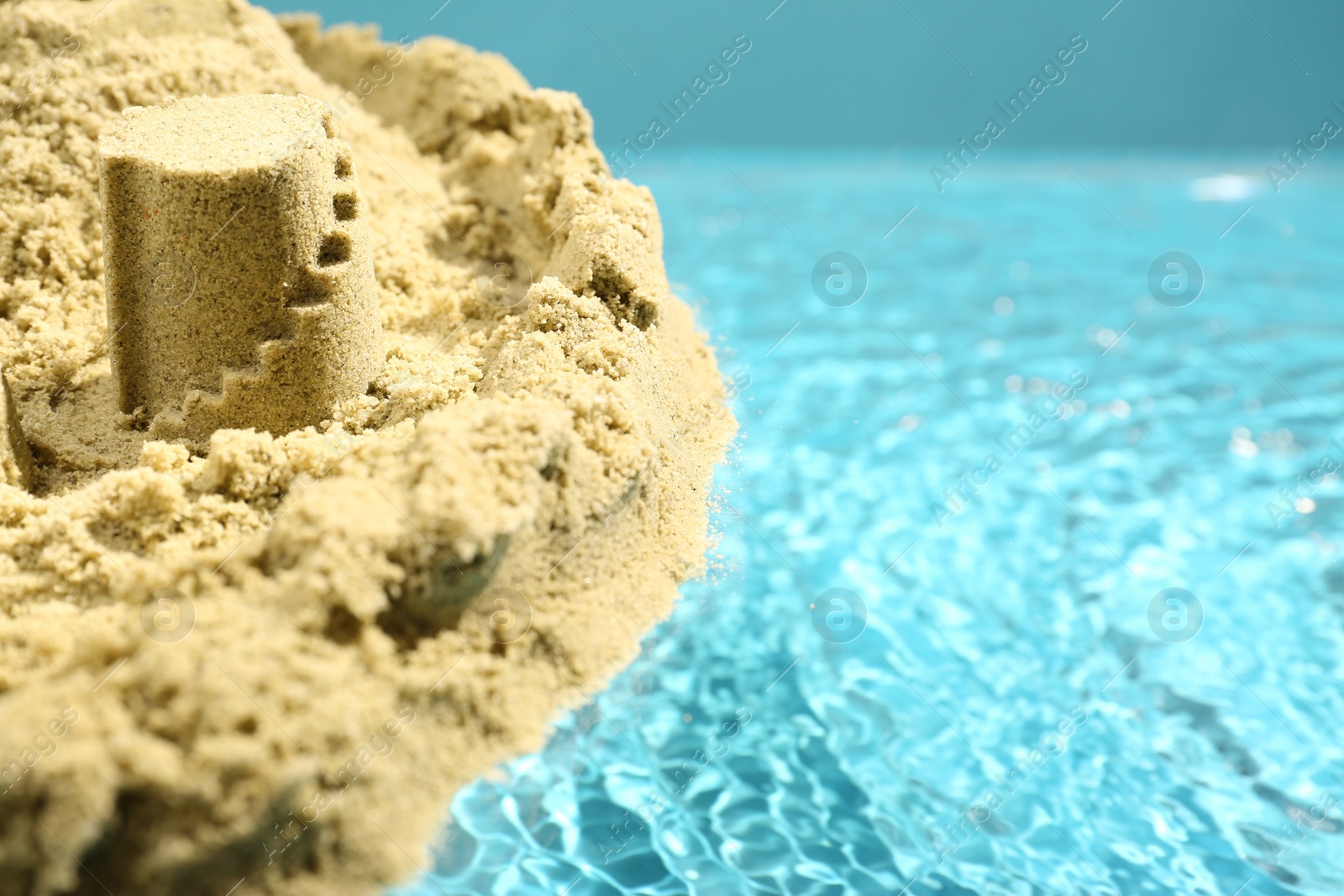 Photo of Pile of sand with beautiful castle on rippled water, closeup. Space for text