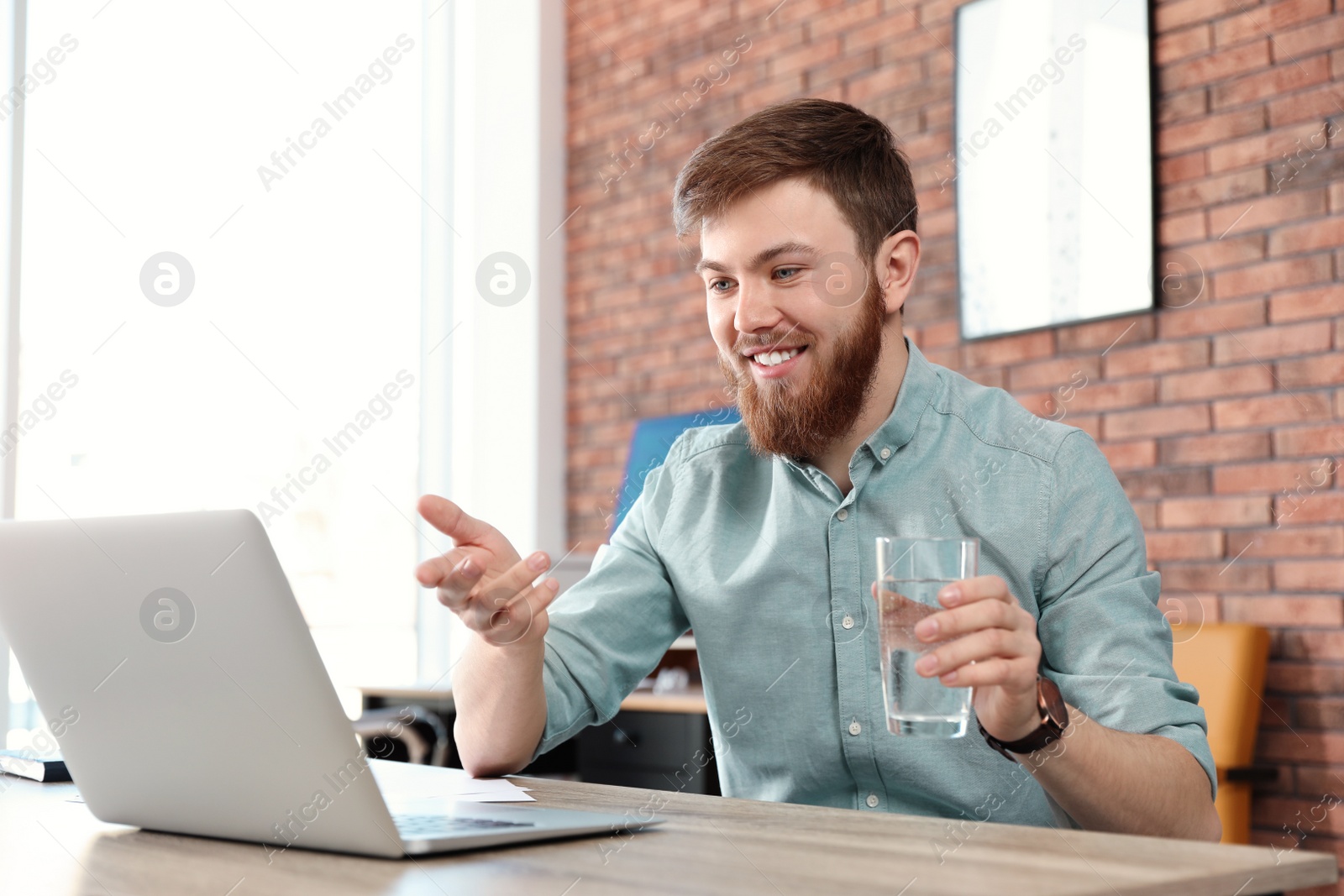 Photo of Young man using video chat on laptop in home office