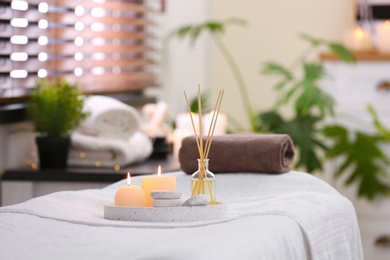 Photo of Composition with reed air freshener, candles and stones on massage table in spa salon