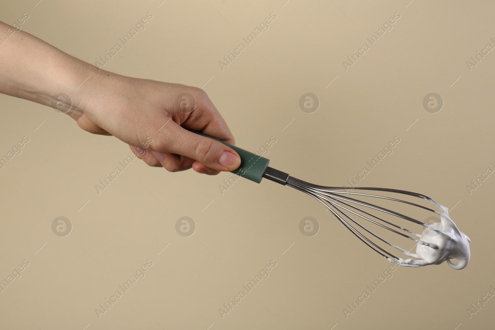 Photo of Woman holding whisk with whipped cream on beige background, closeup