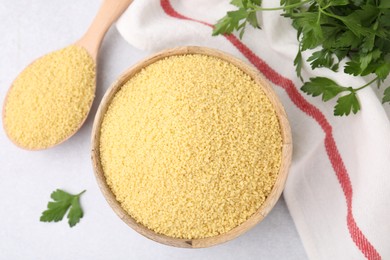 Photo of Raw couscous in bowl, spoon and parsley on light table, flat lay