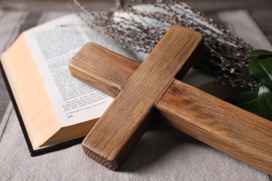 Wooden cross, Bible and willow branches on table, closeup