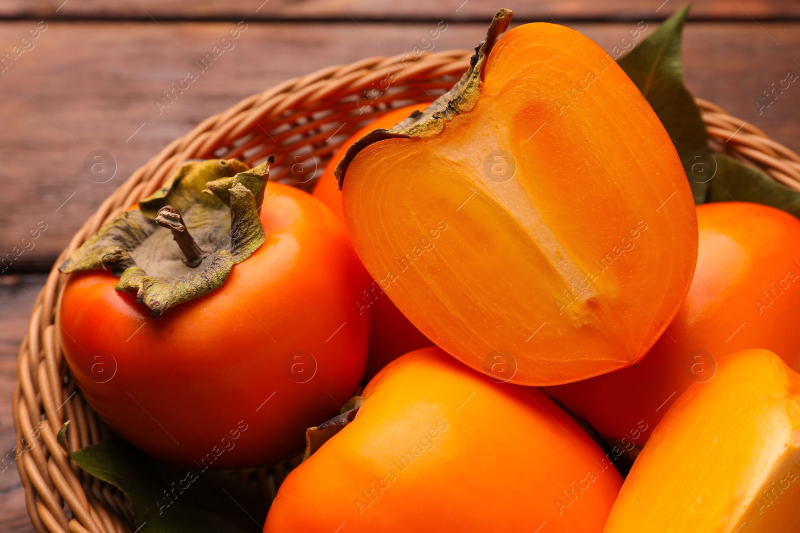 Photo of Delicious ripe persimmons in wicker basket on wooden table, closeup