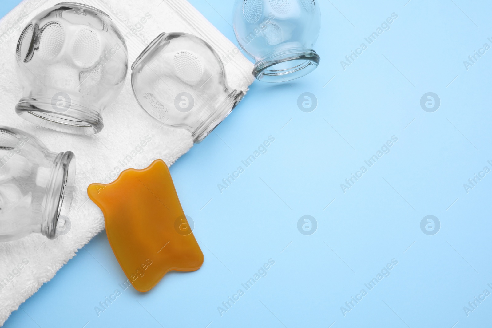 Photo of Glass cups, towel and gua sha on light blue background, flat lay with space for text. Cupping therapy