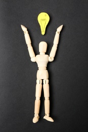 Wooden puppet and paper lightbulb on black background, flat lay