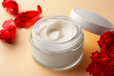 Photo of Jar of face cream and red flower petals on beige background