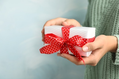 Woman holding beautiful Christmas gift on light blue background, closeup