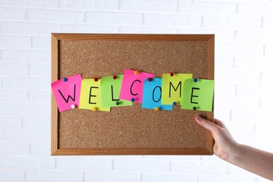 Photo of Woman holding corkboard with word Welcome near white brick wall, closeup