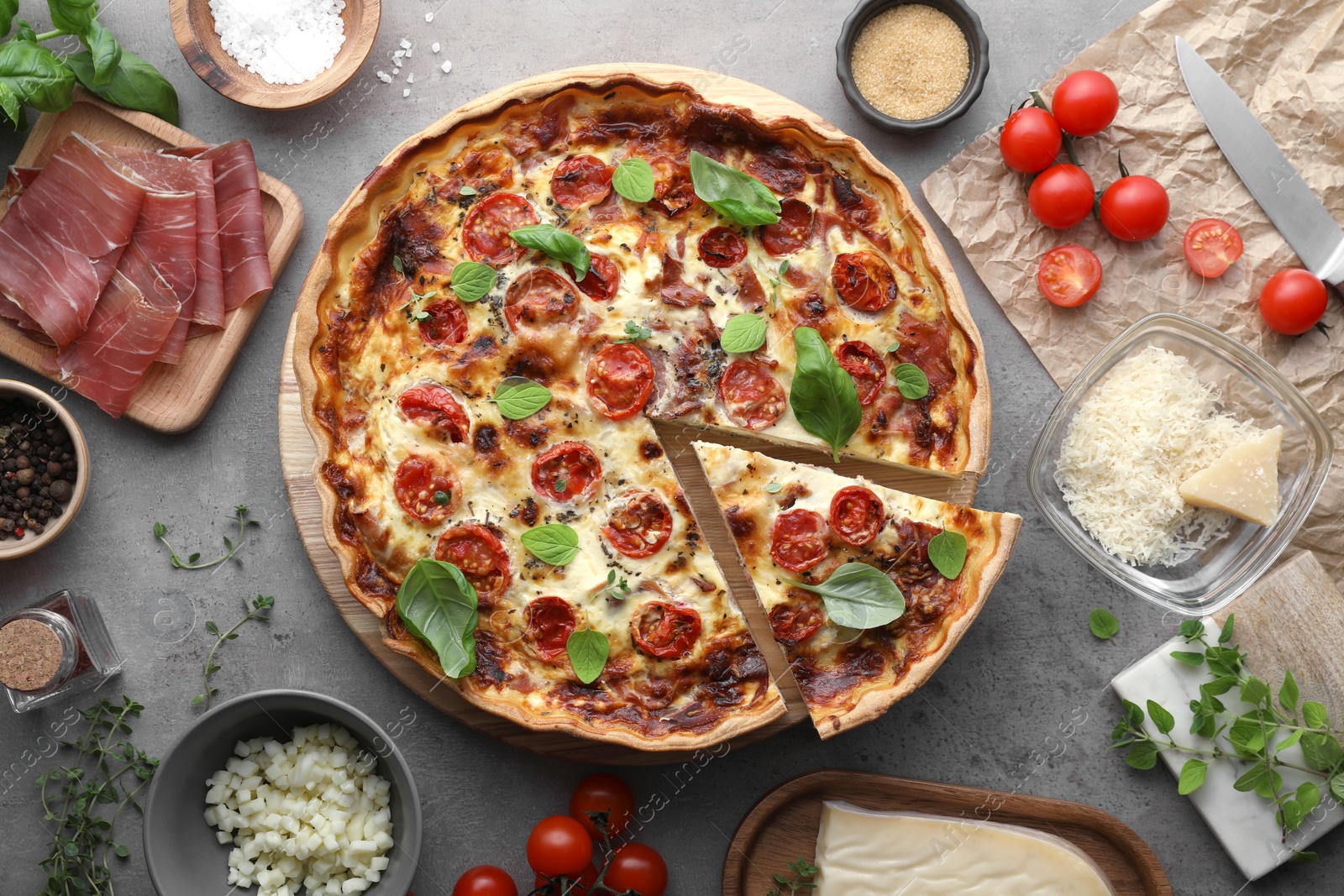 Photo of Cut delicious homemade quiche with prosciutto and ingredients on light grey table, flat lay