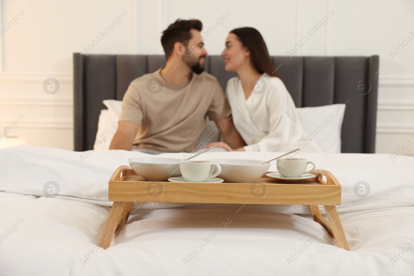 Photo of Happy couple together on bed at home, focus on wooden tray with breakfast