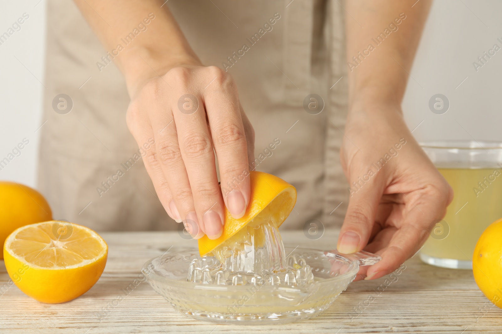 Photo of Woman juicing lemon at white wooden table, closeup