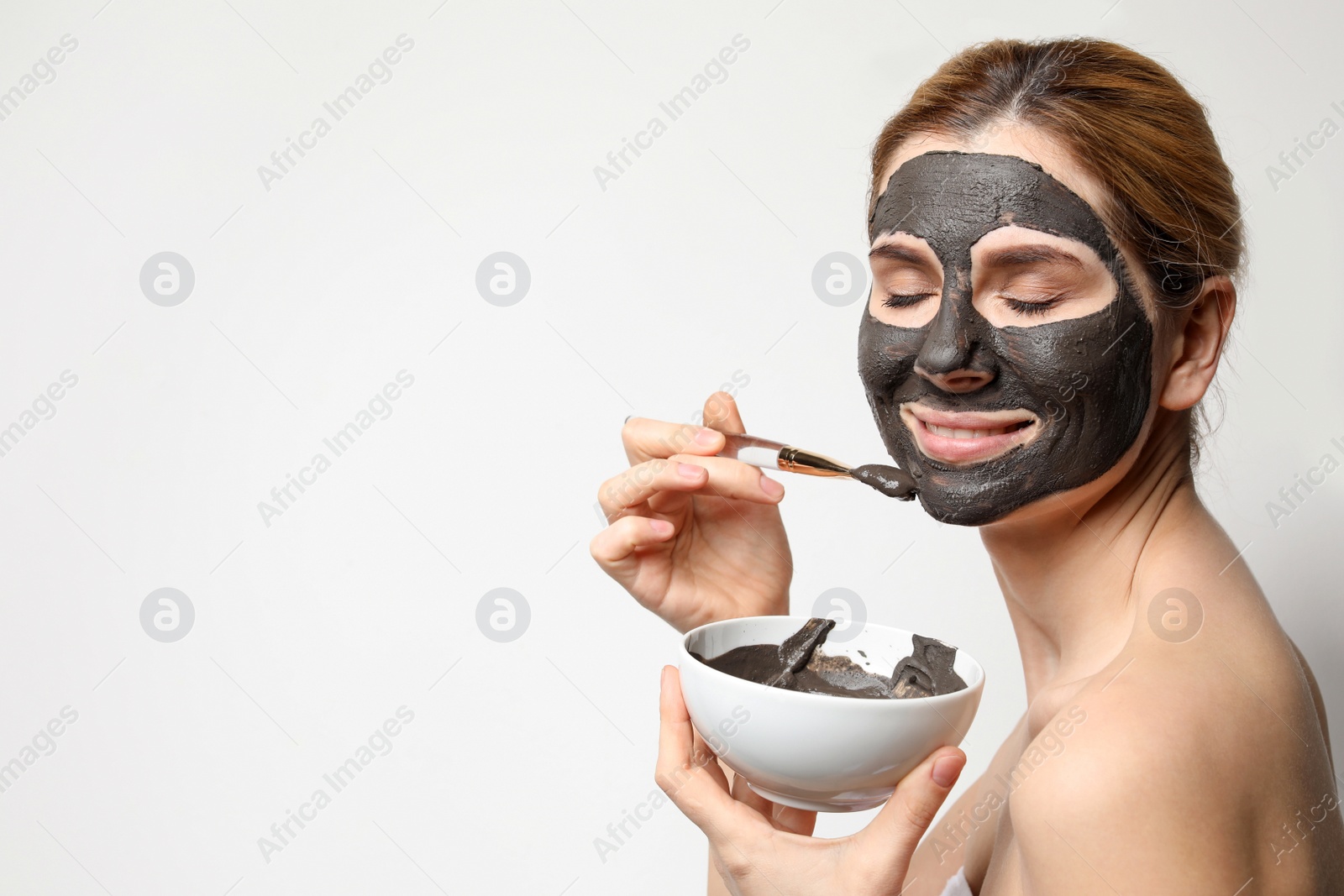 Photo of Beautiful woman applying black mask onto face against light background. Space for text