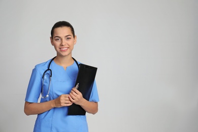 Portrait of young medical assistant with stethoscope and clipboard on color background. Space for text