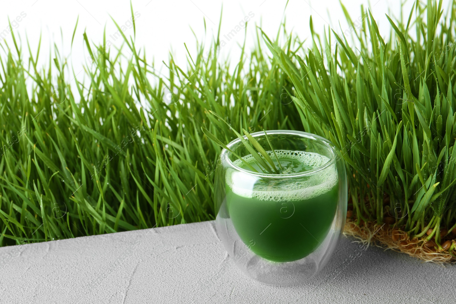 Glass of juice and fresh wheat grass on background. Space for text Photo of Glass of juice and fresh wheat grass on background. Space for text