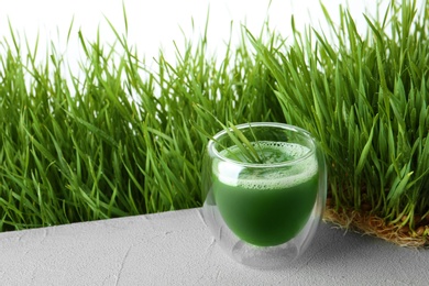 Photo of Glass of juice and fresh wheat grass on background. Space for text
