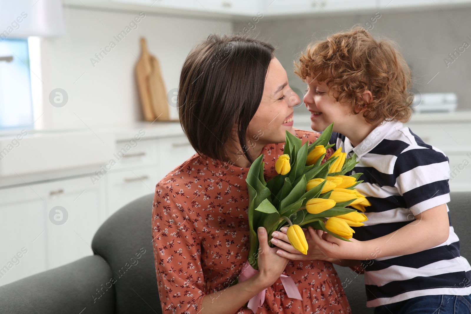 Photo of Little son congratulating his mom with Mother`s day at home. Woman holding bouquet of yellow tulips