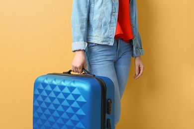 Young woman with suitcase on color background