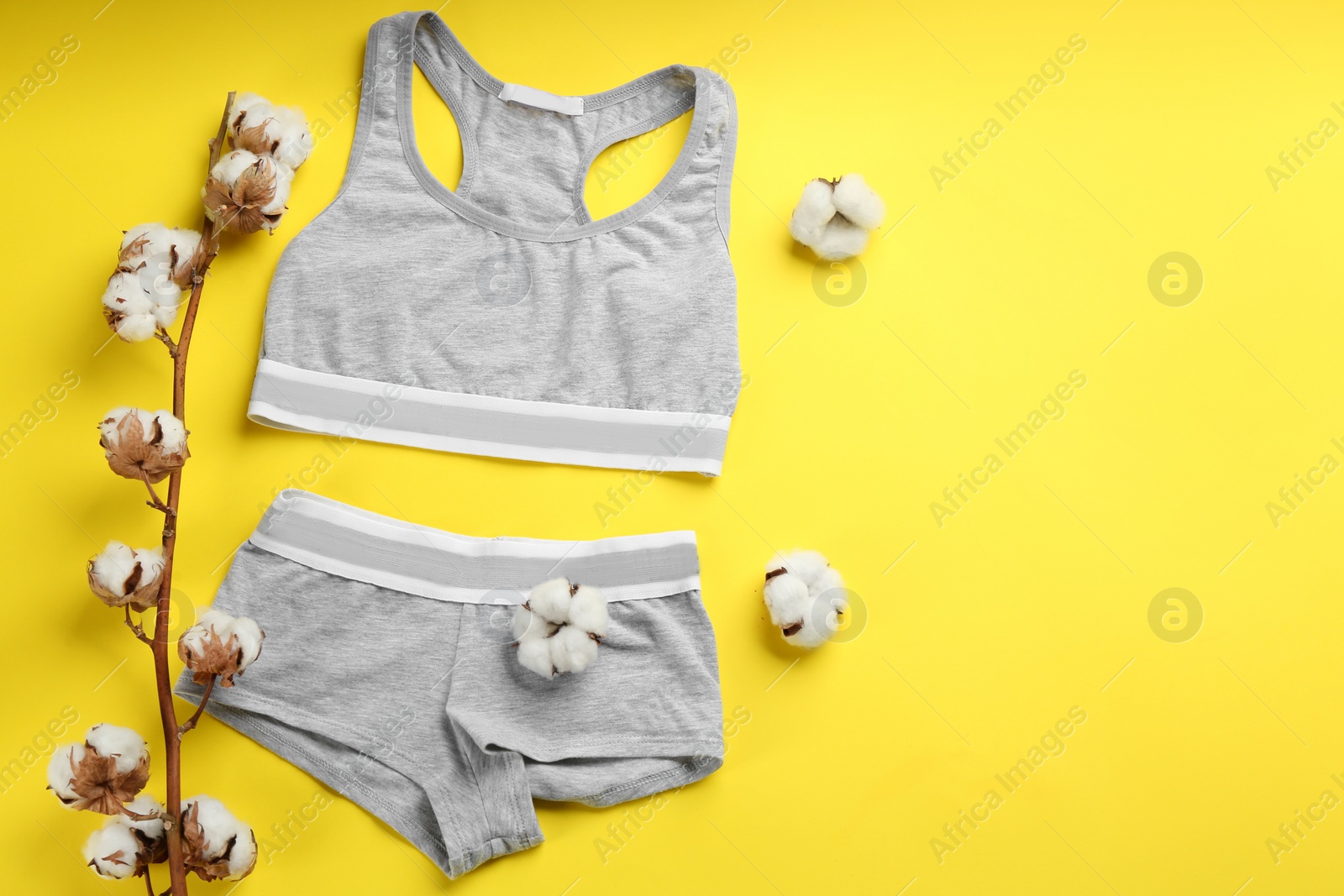 Photo of Sports women's underwear and cotton flowers on yellow background, flat lay. Space for text