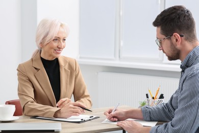 Photo of Happy woman having conversation with man at wooden table in office. Manager conducting job interview with applicant