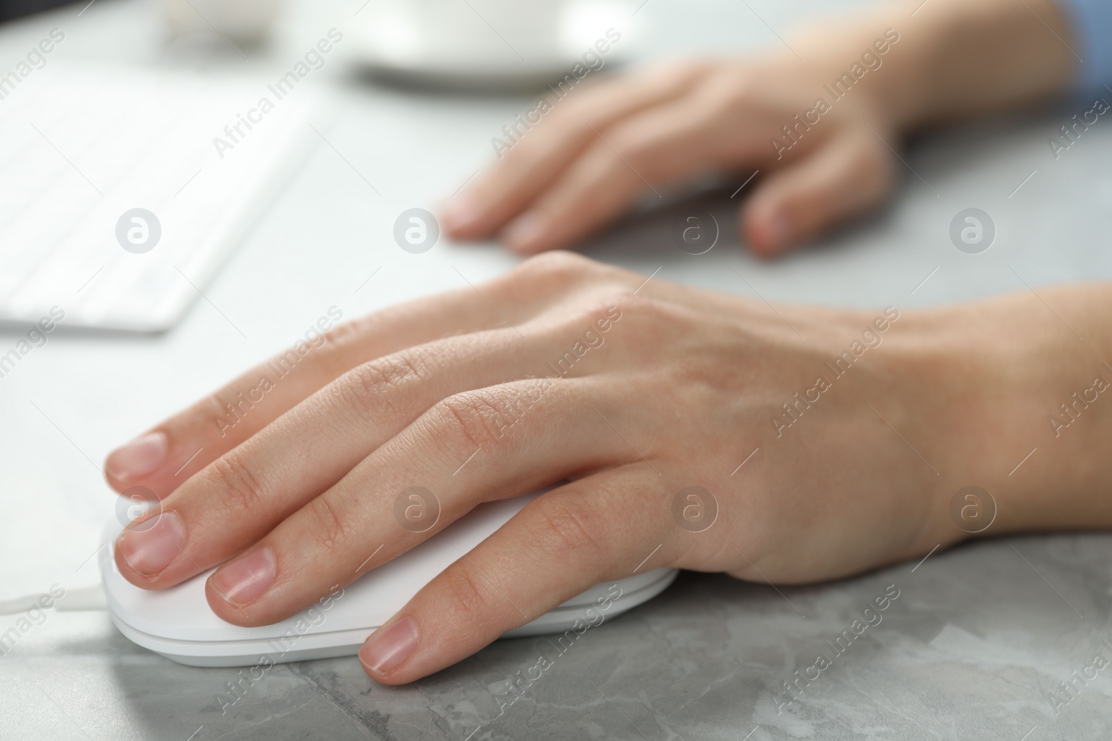 Photo of Woman using wired computer mouse at light grey marble table, closeup