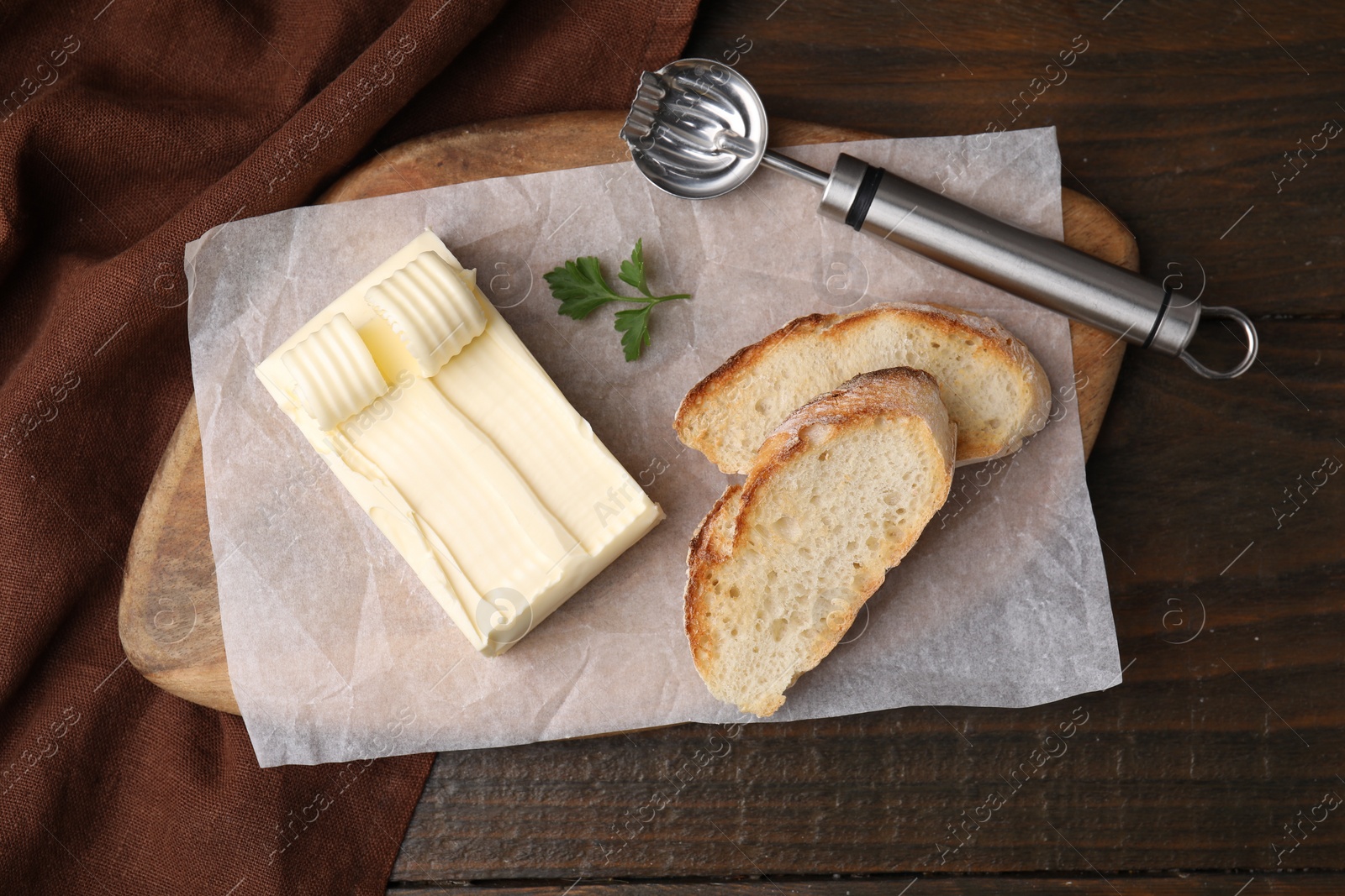 Photo of Tasty butter, slices of bread and spoon on wooden table, top view
