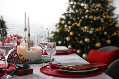 Christmas table setting with burning candles, gift box and dishware indoors