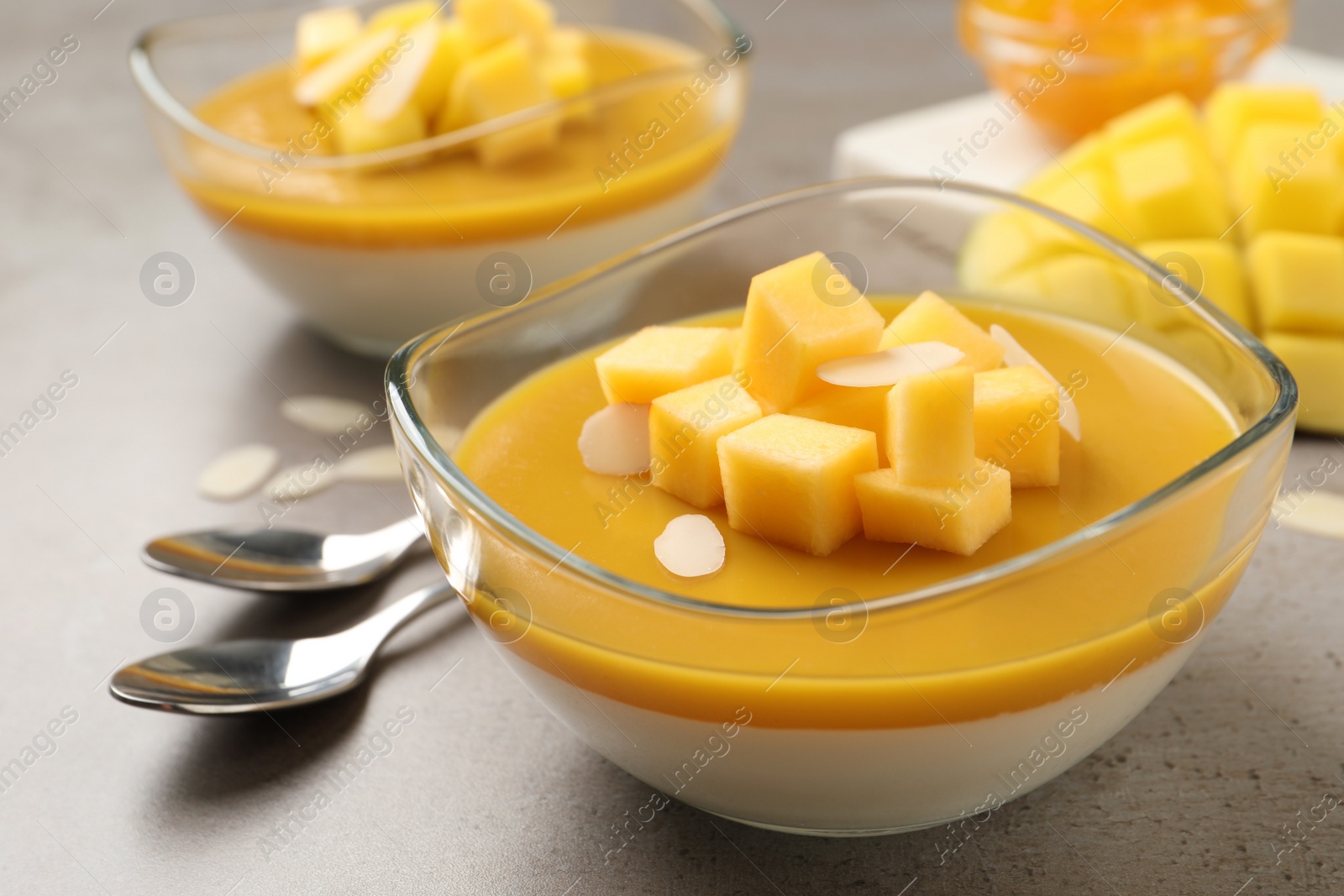 Photo of Delicious panna cotta with mango coulis and fresh fruit pieces on grey table