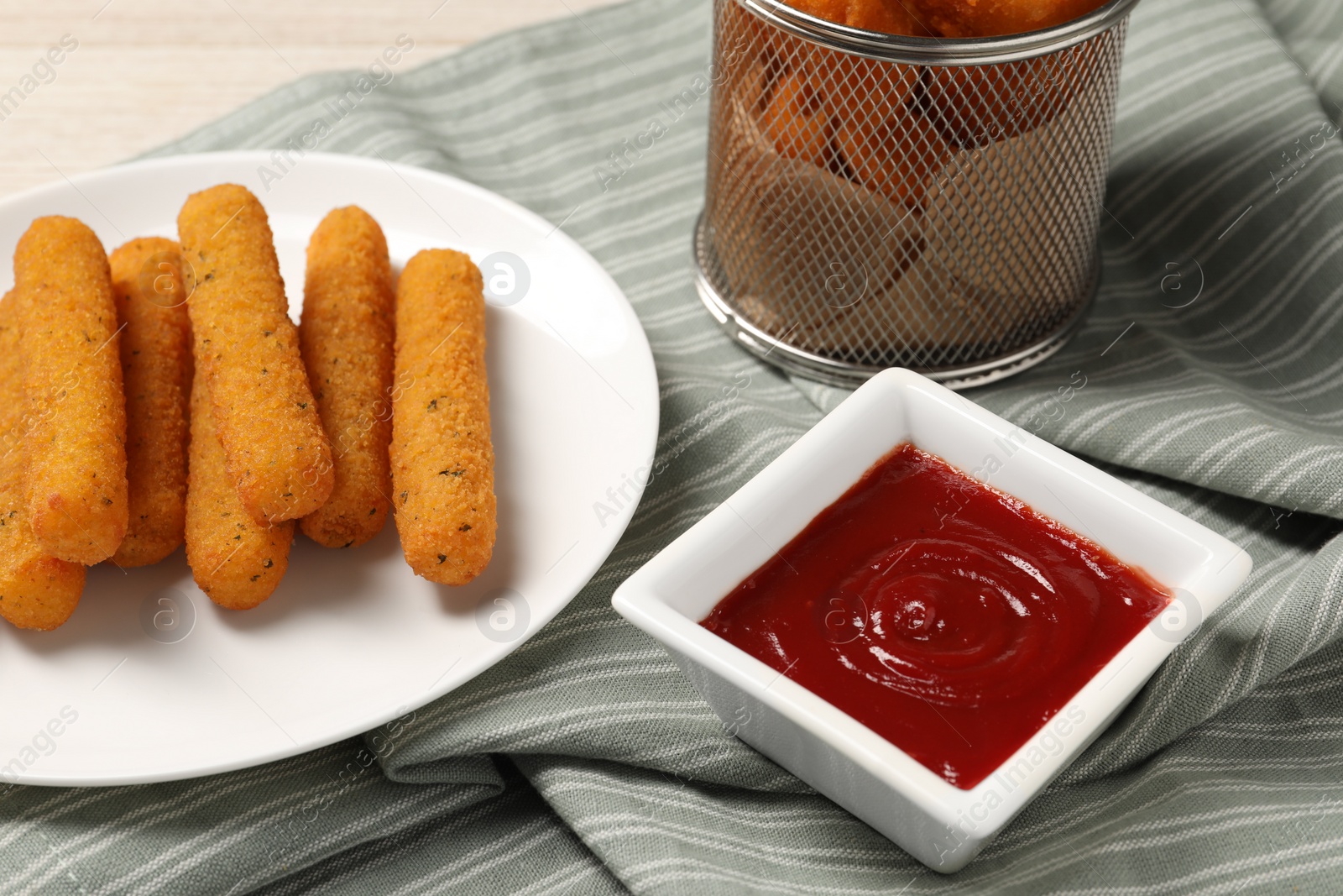 Photo of Tasty ketchup, cheese sticks and chicken nuggets on striped cloth, closeup