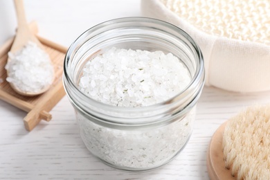 Photo of Sea salt for spa scrubbing procedure in jar on white wooden table
