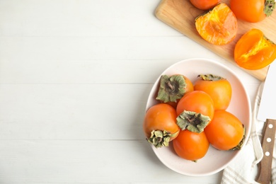 Photo of Delicious fresh persimmons on white wooden table, flat lay. Space for text