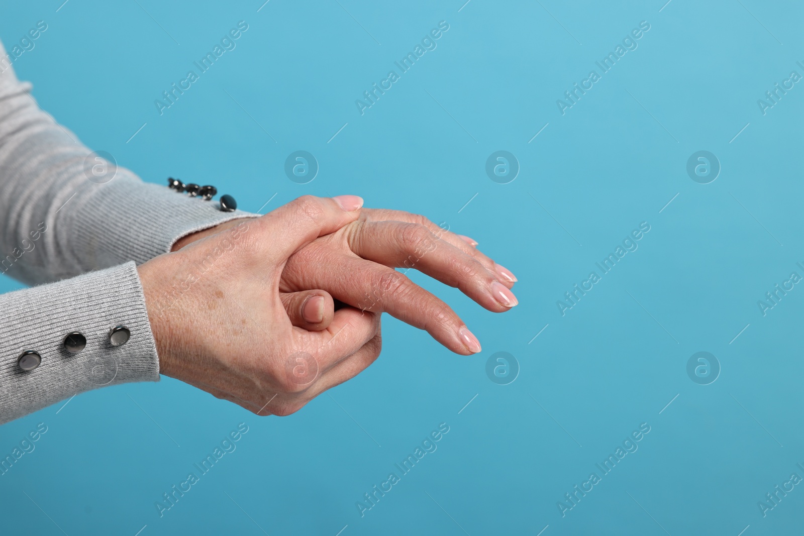 Photo of Arthritis symptoms. Woman suffering from pain in fingers on light blue background, closeup. Space for text