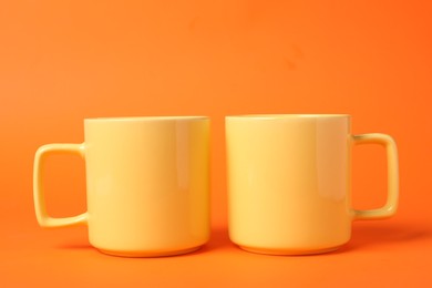 Photo of Two yellow ceramic mugs on orange background