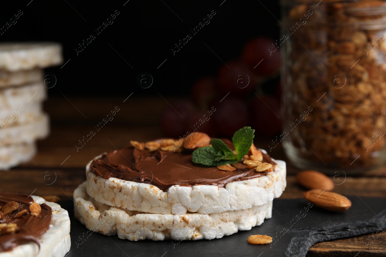 Photo of Puffed rice cakes with chocolate spread, nuts and mint on slate board, closeup