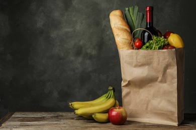 Photo of Paper bag with groceries on wooden table against dark background. Space for text