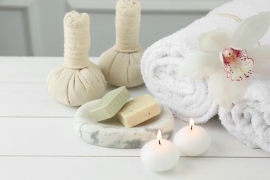 Photo of Beautiful spa composition. Towels, herbal bags, soap bars and burning candles on white wooden table