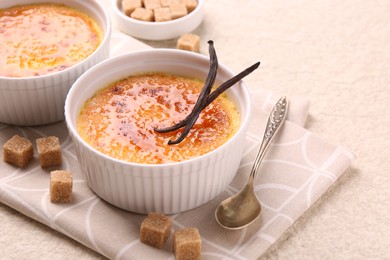 Delicious creme brulee in bowl, vanilla pods, sugar cubes and spoon on light textured table, closeup