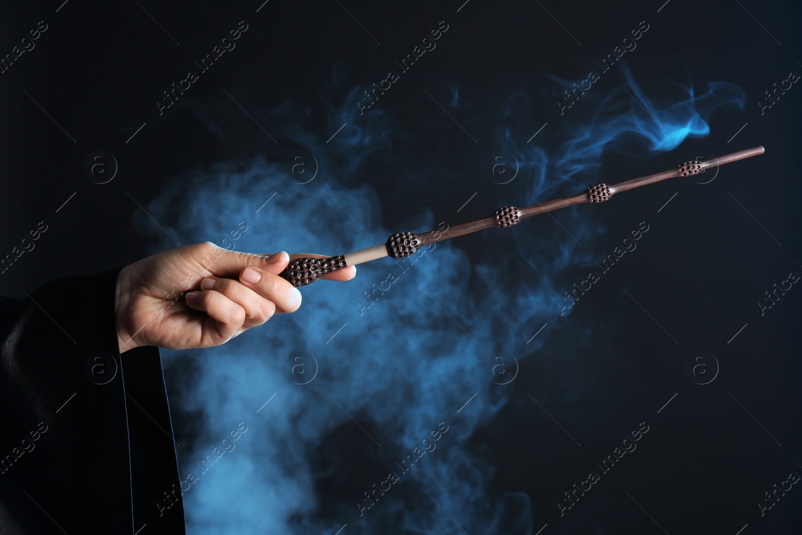 Photo of Magician holding wand in smoke on dark background, closeup