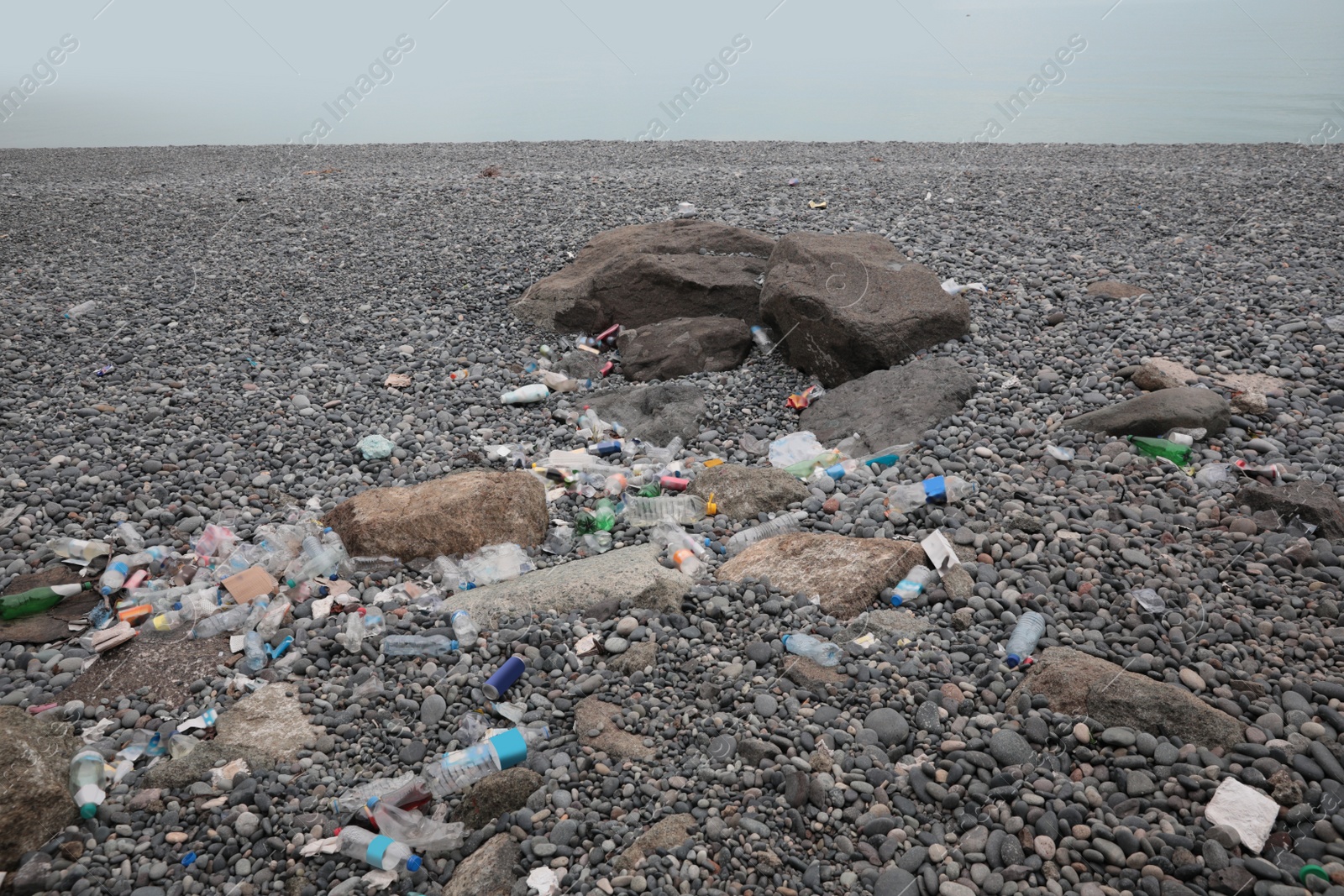 Photo of Garbage scattered on pebbles near sea. Recycling problem