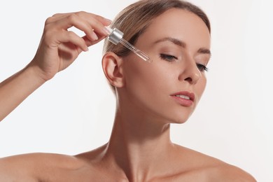 Photo of Beautiful woman applying cosmetic serum onto her face on white background