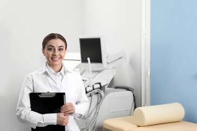 Professional sonographer with clipboard near modern ultrasound machine in clinic