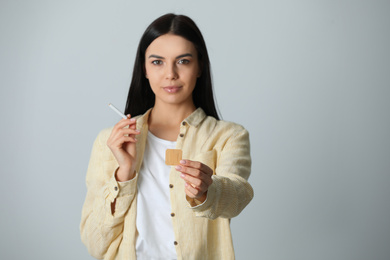 Photo of Happy young woman with nicotine patch and cigarette on light grey background