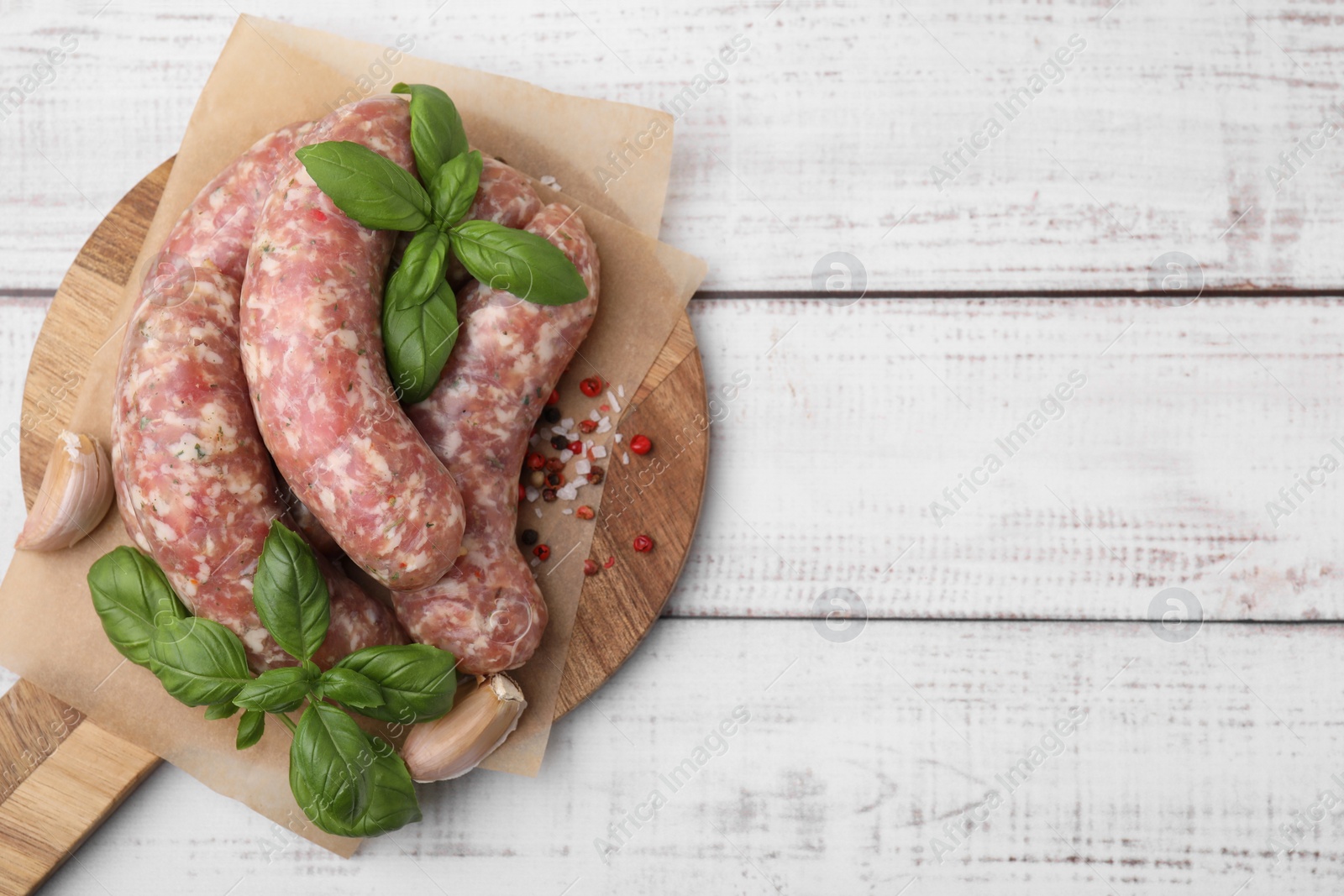 Photo of Raw homemade sausages and different spices on white wooden table, top view. Space for text