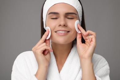 Photo of Young woman cleaning her face with cotton pads on grey background, closeup